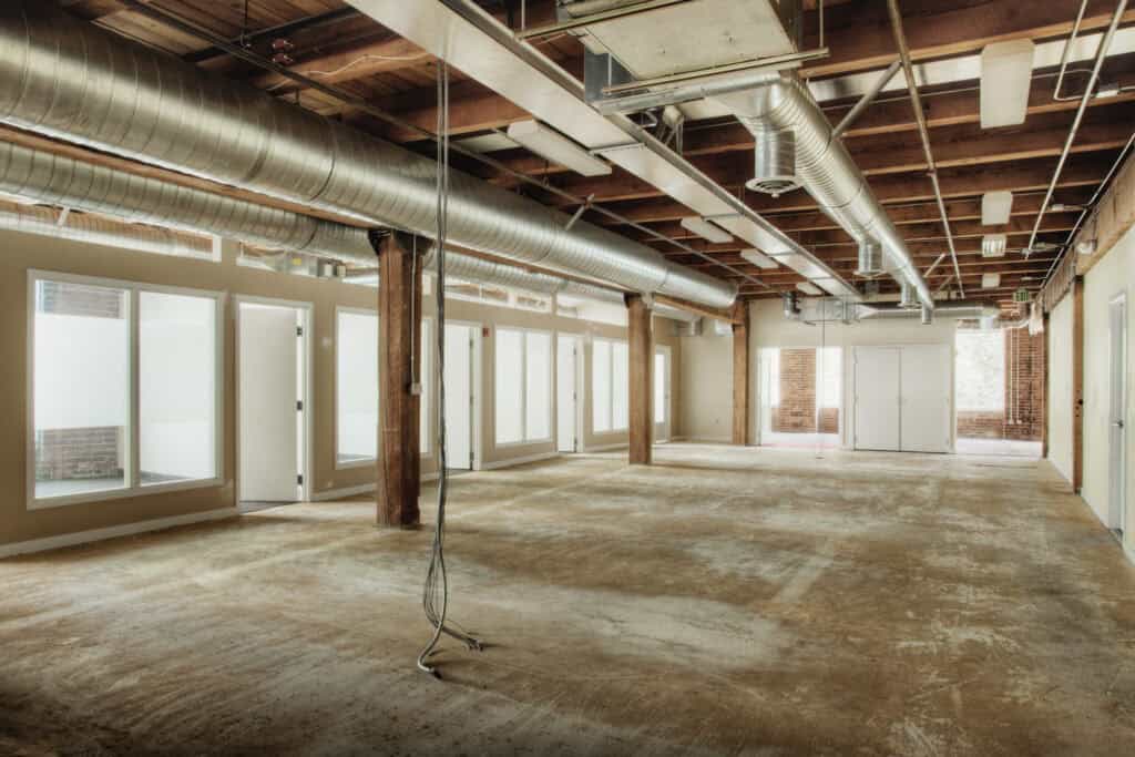 Spacious commercial interior under renovation with exposed ductwork and large windows.