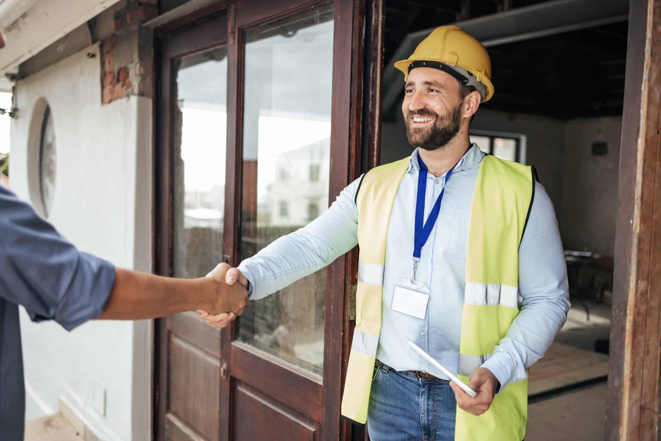 Construction worker shaking hands with client at site, wearing safety gear.