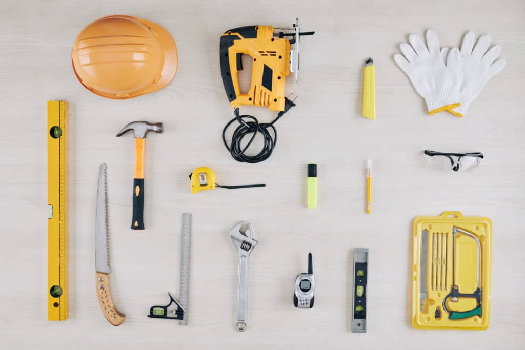 Assorted construction tools and safety gear on a light wooden surface.