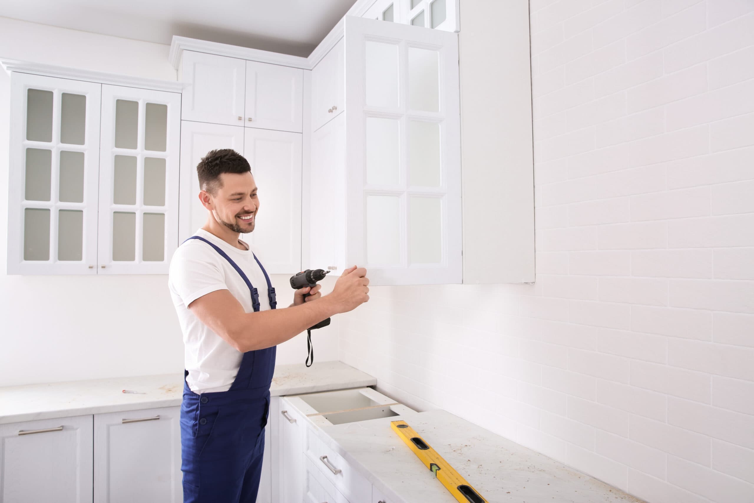 Skilled worker installing kitchen cabinets in a modern white kitchen.