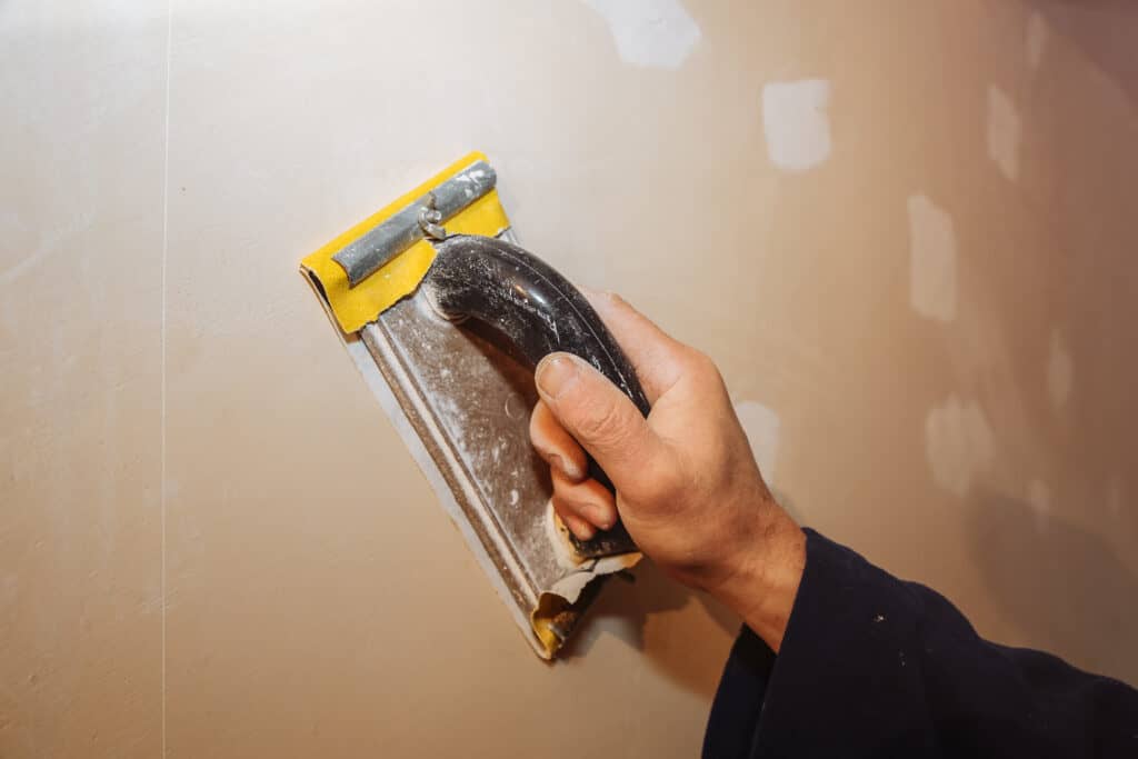 Person sanding drywall with a hand sander for smooth wall finish.