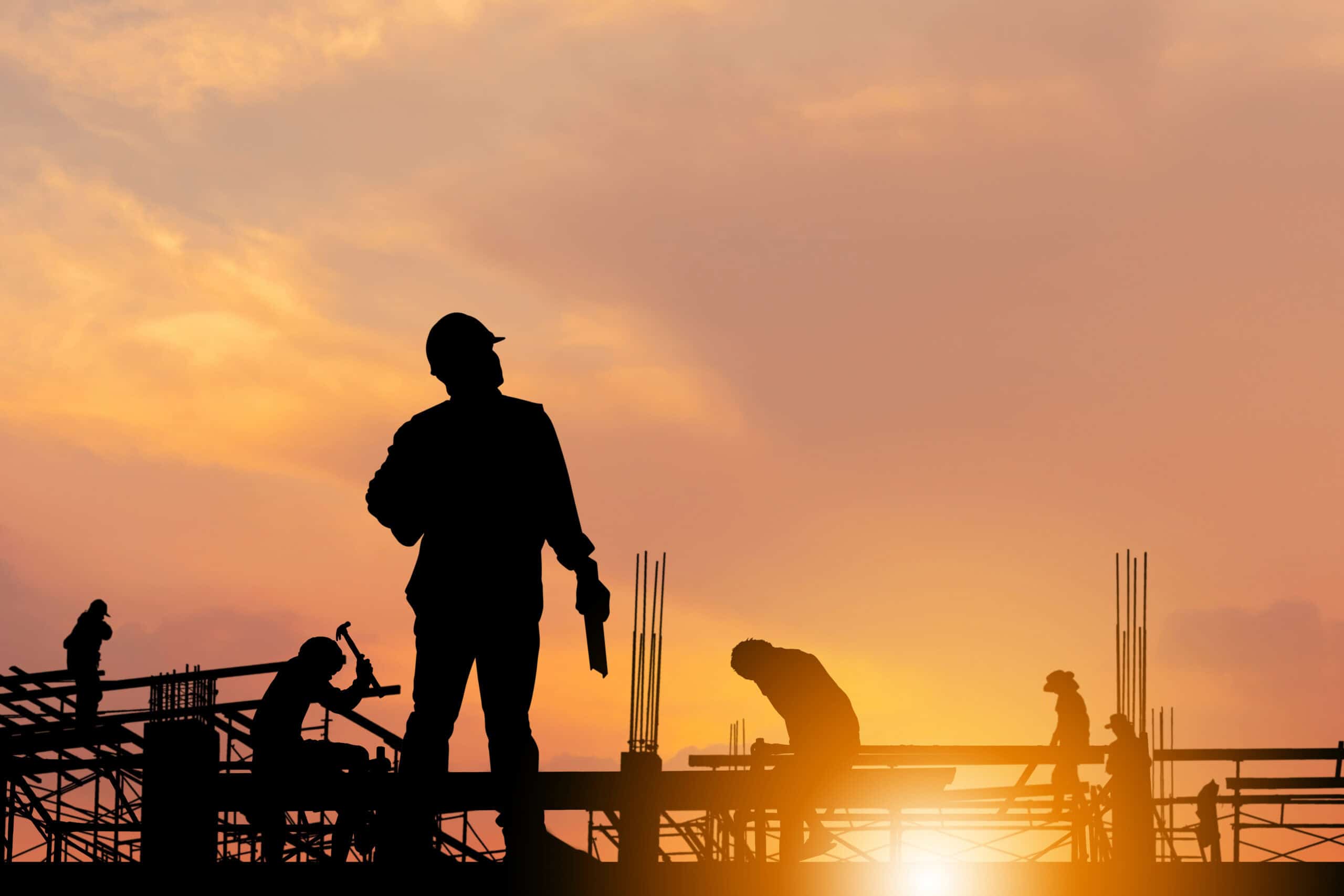 Construction workers building at sunset with silhouetted figures.