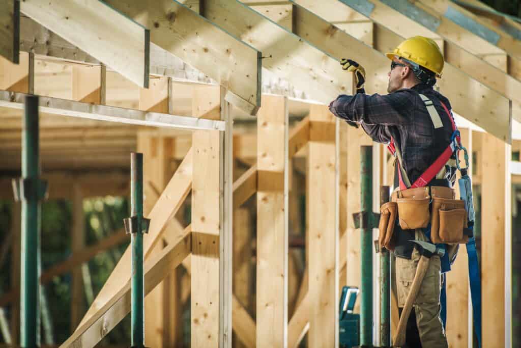 Construction worker in safety gear working on wooden framing at a construction site.